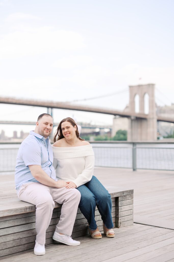 Couple holding hands looking at camera with Brooklyn Bridge behind them
