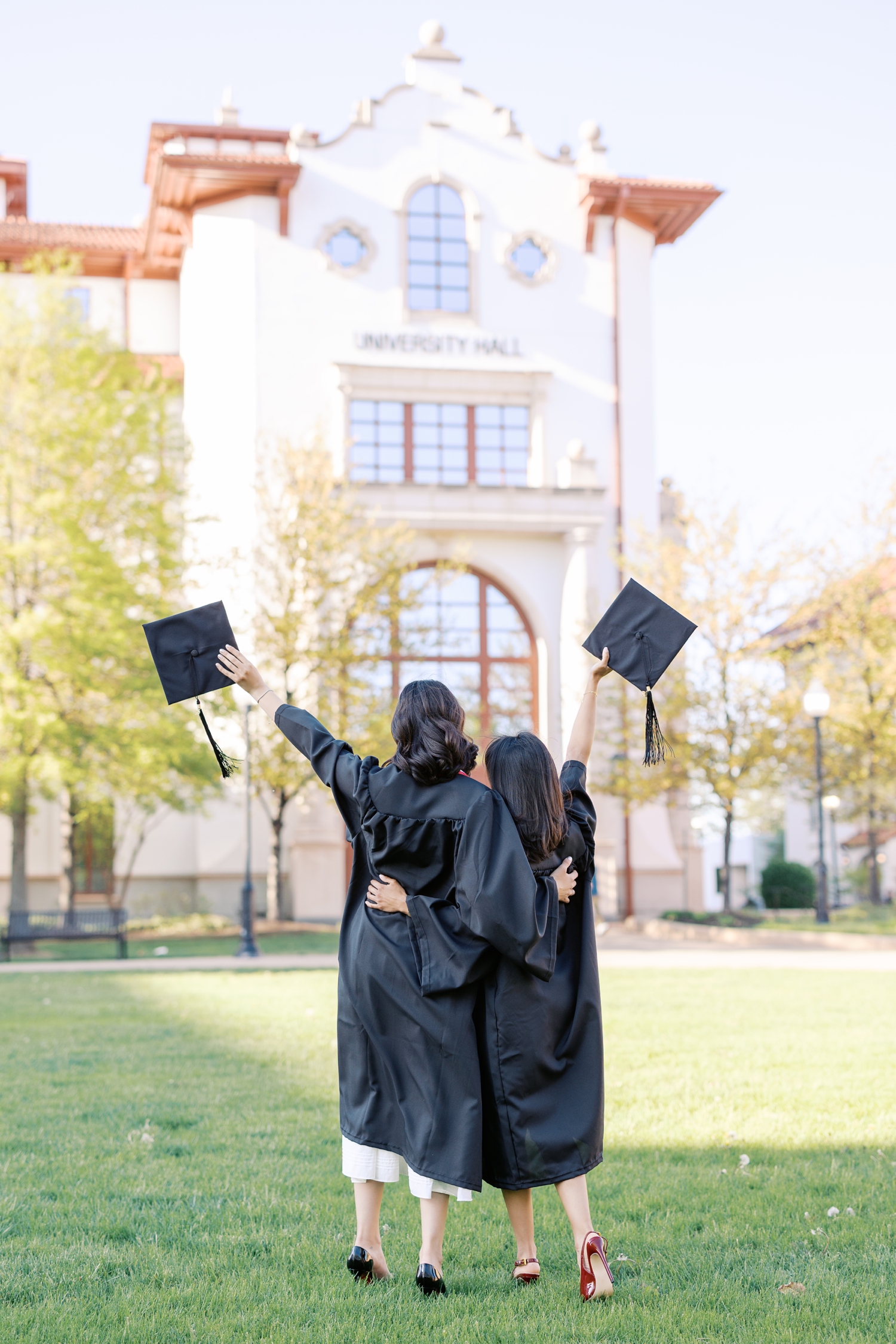 Two girls holding up cap and gown in front of academic building at Montclair State University in New Jersey
