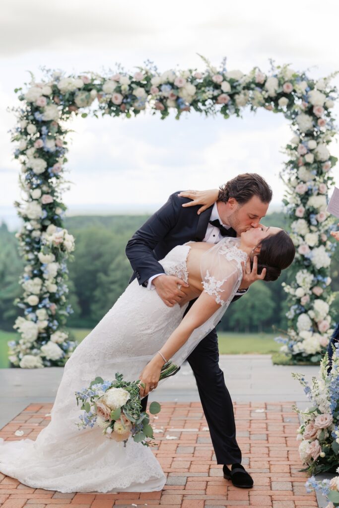 Bride and groom share a dip kiss beneath a floral arch at their Pendry Natirar wedding in New Jersey